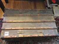 Top and partial front view of vintage steamer trunk showing wooden slats, metal rivets, and worn leather handles