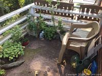 Corner with over 10 live plants in assorted pots, two beige plastic stackable patio chairs, garden ornaments including small statue.