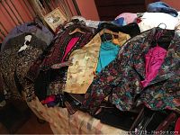 Group of vintage ladies garments including jackets, camisoles, pants, and blazers arranged on a bed and nearby surfaces