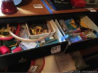 Open drawer showing divided compartments with multiple sewing supplies including embroidery hoops, spools of thread, ribbons, and scissors.
