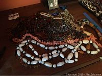 Overview of multiple necklaces showing variety in beads and color including coral, amber, hematite, white carved shell, and others.