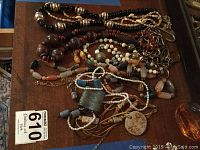 Top view of multiple assorted costume jewelry necklaces laid out on a surface showing variety of materials such as wood, stone, faux pearl, and seashell.