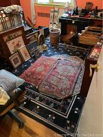 Room corner with black floral border large rug underneath two traditional Persian rugs in red tones, and an octagonal muted pattern rug partially visible