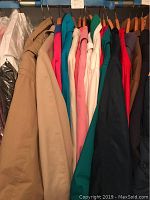 Front view of various women's coats hanging on rack in multiple colors including tan, pink, blue, teal, white, black, and red.