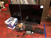 Wide view of the Panasonic Viera TV with remote, Sony Dream Machine clock radio box, other clock radios, portable TVs, and Plantronics gaming headset box all together on floor.