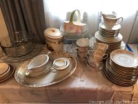 Overview of the entire lot showing a large glass divided candy dish, ceramic floral tulip basket, a metal tin container, covered dish, cream pitcher, multiple cups and plates with gold-edged Royal M Valencia pattern.