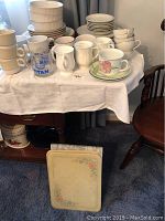 View of Mikasa Country Classics plates, bowls stacked with various mugs on table and cutting boards below.