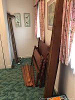Two sets of twin bed frame components including headboards, footboards, wood side rails and slats, stacked against wall in narrow room.
