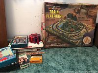 Photo showing MiNibase Train Platform box with artwork and multiple vintage board games stacked alongside, including poker chips in a red holder