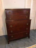 Front view of vintage wooden chest of drawers with two sections and brass handles.