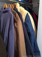 Photo showing multiple jackets hanging on a rack including purple hoodie, beige trench coat, blue puffer jacket and tan jacket