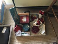 Two trays with various home decor items and boxed cutting set on floor
