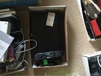 Top view of the Cisco Nextbox with remote and cables inside a box on the floor.