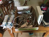 Photo of Nintendo Wii console and multiple accessories including two Wii remotes, two nunchuks, and cables inside a box.