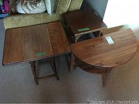 Top view of three wooden tables placed together on carpet showing different shapes and wood finishes including demi-lune, drop leaf and three shelf designs.