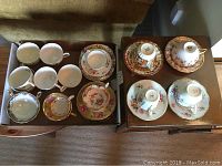 All tea cups and saucers arranged in two boxes showing different floral and gold designs.