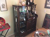 Front view of vintage wood display cabinet showing glass display section, drawers, and upper shelves with glassware.