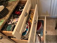 Open drawers showing an assortment of plates, bowls, cookware, and storage containers, some with lids.