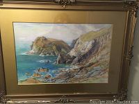 Close-up front view of the framed watercolour artwork showing coastal cliff and water scene with ornate decorative frame and tan matte.