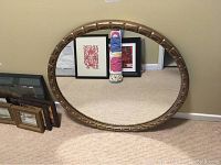 Front view of round mirror with decorative gold frame and clear reflective glass, showing part of the surrounding room.