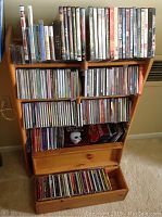 Front view showing the wooden stand filled with DVDs on top shelves and CDs in lower shelves and drawer, drawer partially open showing additional CDs and a wooden box