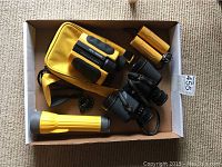 Top view of the lot showing binoculars, carrying case, sports glasses, a yellow Lumilite flashlight, and a small yellow pocket flashlight in a cardboard box.