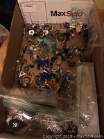 Top view of first tray showing assorted pierced and screw back earrings and several rings in plastic bags scattered within the box