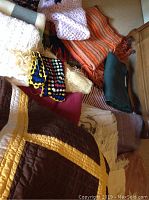 Full view of various blankets and knitted afghans in assorted colors and textures, showing multiple items including crocheted, knitted, and woven pieces