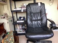 Front view of black leather-look office chair showing padded backrest and seat, armrests, and part of the base with wheels visible.