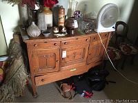 Front view of wood buffet with decorative carved panels and various items on top. Shows areas of wear and loose hardware.