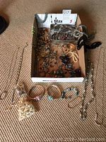 Photo showing a box filled with assorted earrings, rings, chain necklaces, and bracelets, along with additional jewelry pieces laid out around the box.