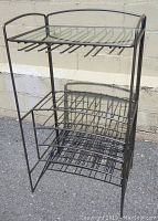 Front view of black metal wine rack showing two wine bottle storage tiers and glass top shelf with stemware hanging rack.