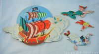 Photo shows four flat illustrated Disney Peter Pan pin-up toys on light blue background, including pirate ship, Peter Pan flying figure, Tinkerbell fairy, and Michael John figure.