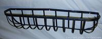 Full view of black metal planter holder showing rectangular frame, vertical and curved support bars. Weathered look and tie straps holding some bars in place.