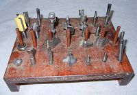 Top angle showing over 20 different router bits of varying shapes and sizes in a wooden holder.