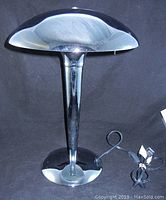 Front view of chrome lamp showing dome-shaped metal shade, tapered stem, and round base with attached power cord.