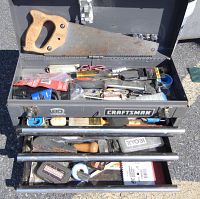 Open view of gray Craftsman steel toolbox filled with various hand tools including a hand saw with wooden handle, screwdrivers, utility knife, Ryobi box, tape, and other tools.