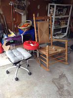 Black swivel chair with grey cushion, red stool, and wooden rocking chair with woven seat and visible detached arm piece lying on same seat.