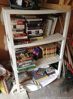 White plastic shelving unit with multiple stacks and rows of books including encyclopedias and other assorted books.