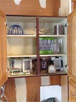 Open cabinet showing blue plastic bowl, silver metallic bowl, set of clear plastic champagne flutes in original box, several photo frames, wreath and small decorative items.