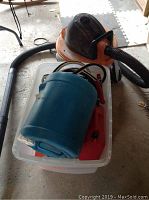 Plastic bin containing booster cables, two red gas cans, and blue water container