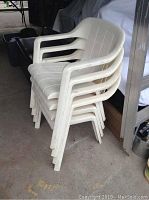Four stacked white plastic lawn chairs showing side and top view, placed in storage area.