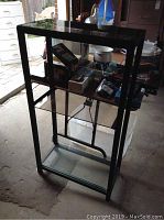 Full view of the metal frame and four glass shelves showing contents on shelves and wear.