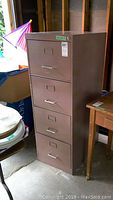 Full view of beige metal filing cabinet with all drawers closed, showing four drawers with handles and label holders.