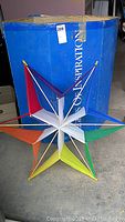 Front view of multi-colored Flights of Inspiration star kite showing triangular fabric sections supported by rods in red, purple, orange, white, blue, green, and yellow colors.