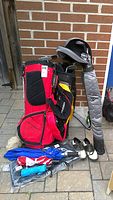 Full view of golf bags, golf shoes, and golf umbrellas arranged on patio with brick wall backdrop.