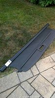 Black rear cargo cover, extended horizontally on grass and pavement, showing full length and handle in center.