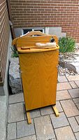 Front view of wooden portable press with brush on top and base feet for stability on stone patio