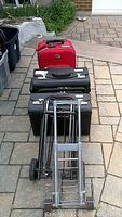 Full view of all items showing the red carry-on, two black briefcases, and two metal luggage carts lined up on pavement.