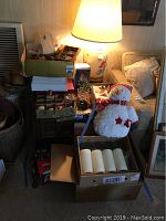 Overall view of the lot showing stacked Christmas decorations, gift boxes, plush snowman, candles, wicker baskets, and a lamp on side table (lamp and table not included).